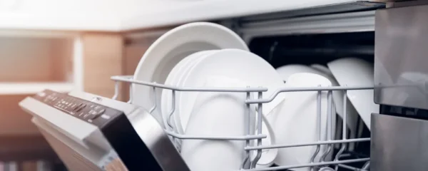 Personne chargeant un lave-vaisselle moderne dans une cuisine contemporaine, organisant soigneusement la vaisselle dans les paniers.