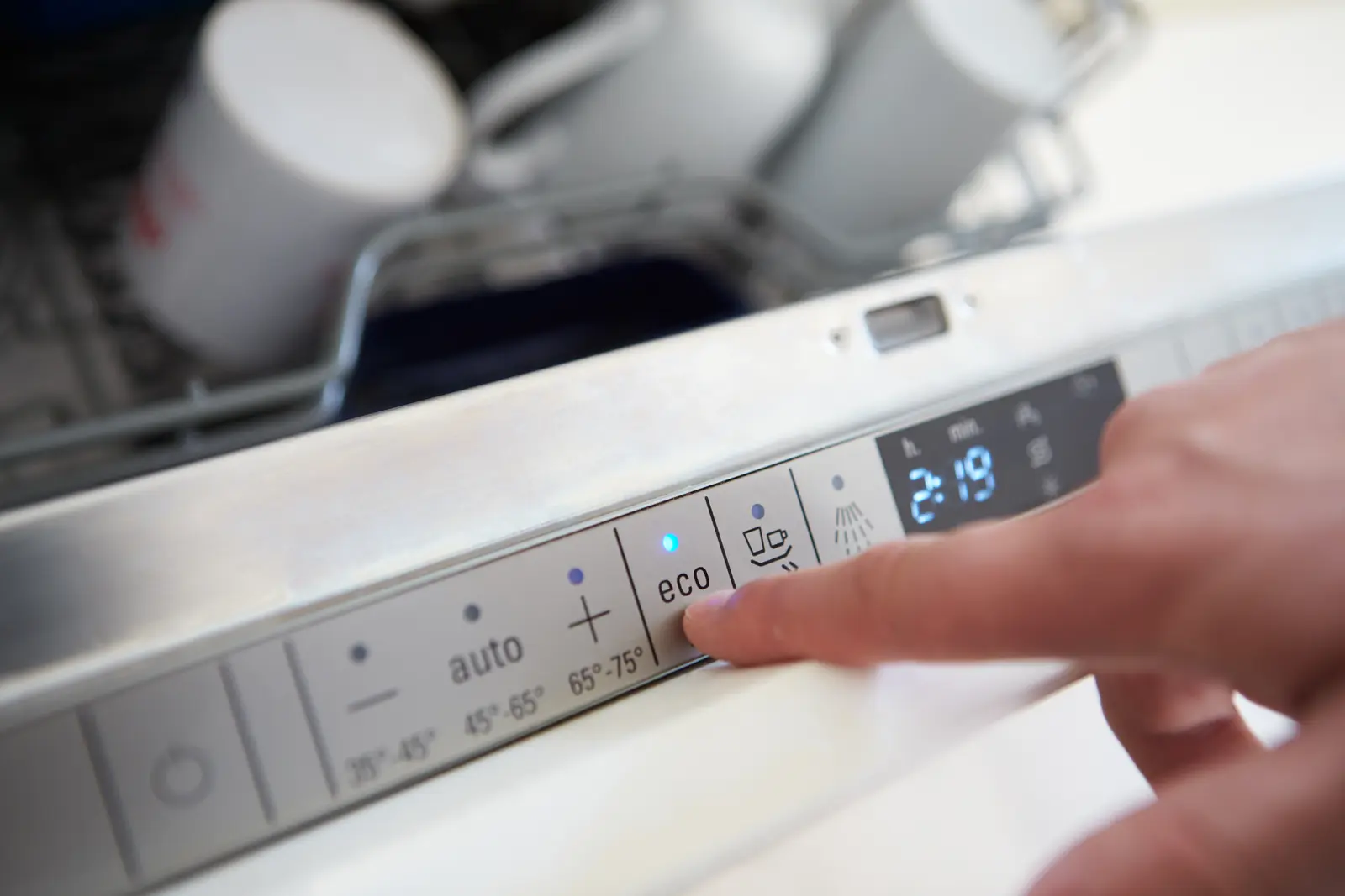 Main appuyant sur le bouton programme Éco d'un panneau de commande de lave-vaisselle moderne.
